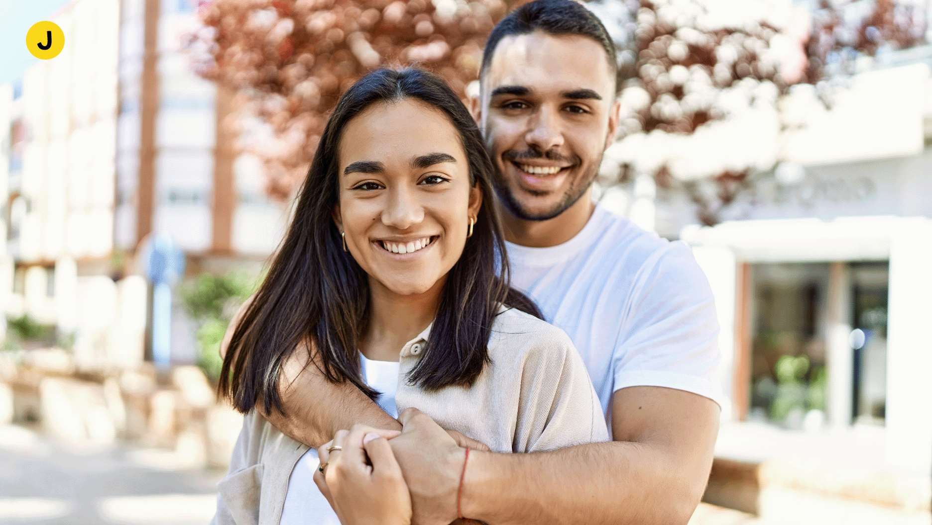 J. Une femme et un homme se font un câlin en souriant à la caméra.