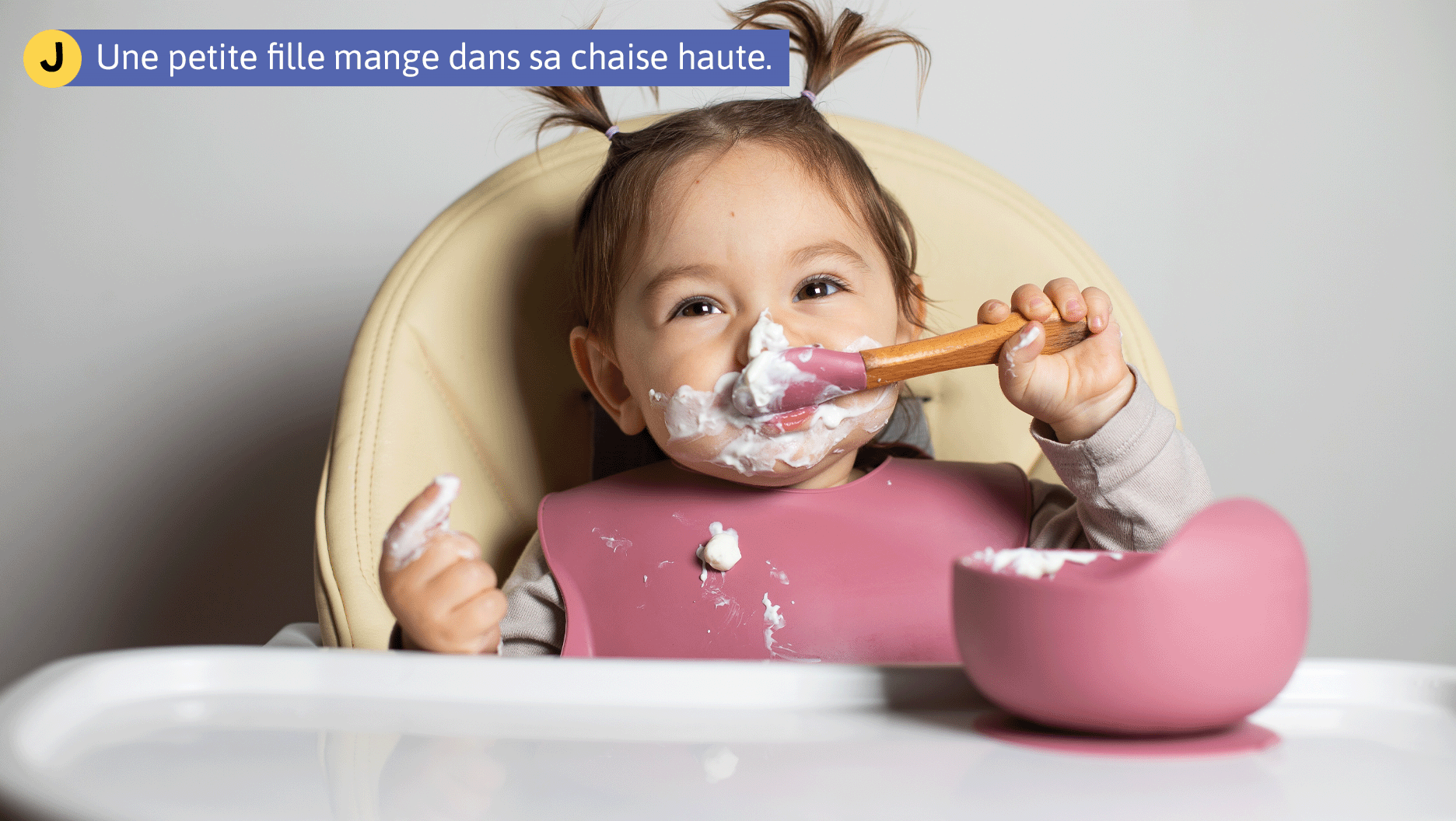 Une petite fille mange dans sa chaise haute.