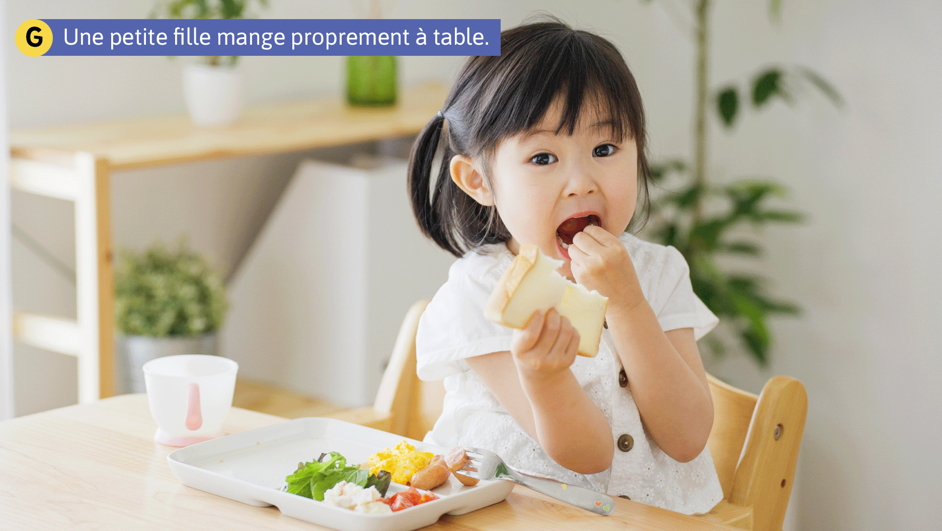 Une petite fille mange proprement à table.