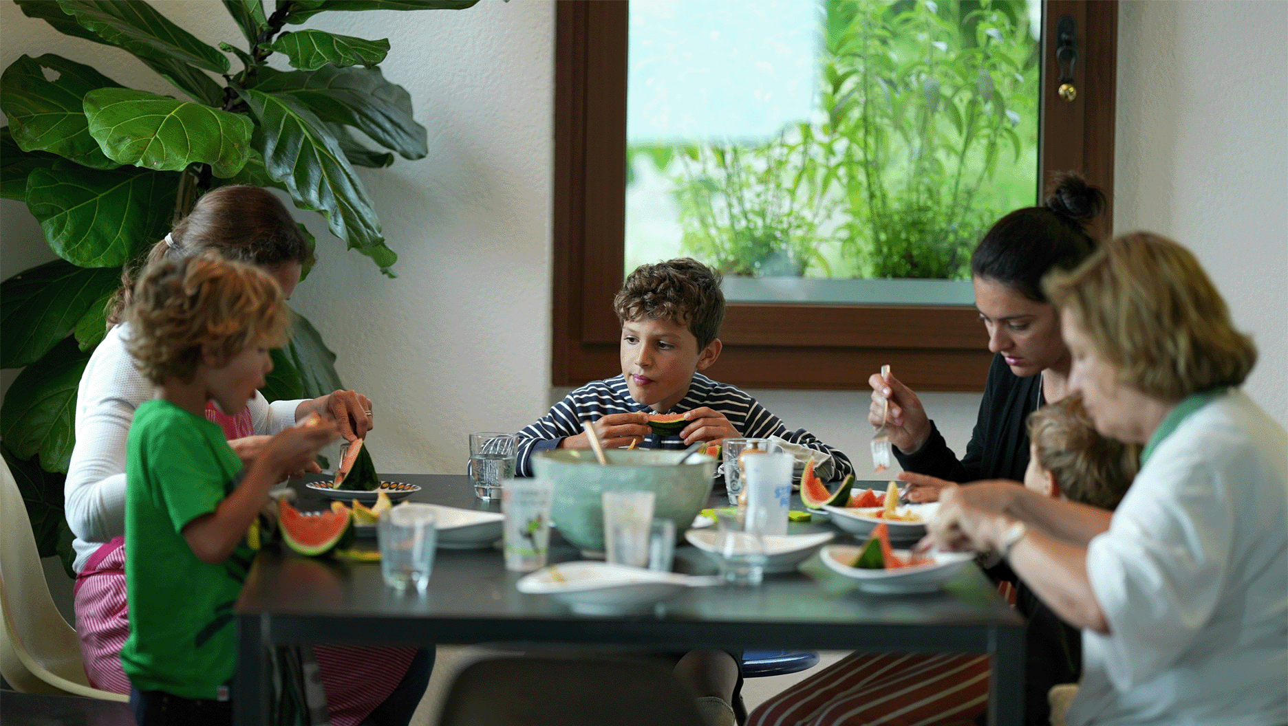 Une famille à table mange de la pastèque.