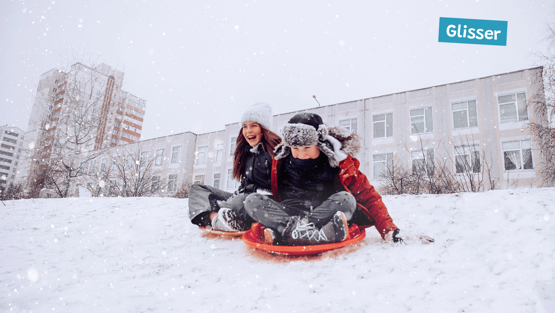 Deux jeunes, assis sur des soucoupes, glissent sur la neige.